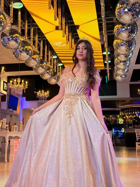 Quinceañera con vestido dorado bajo las bolas de espejos del salón